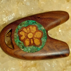 May include: A wooden, U-shaped object with a carved flower design inlaid with turquoise and gold stones.