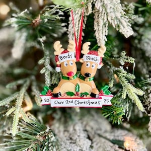 May include: A Christmas ornament featuring two reindeer with the names "Brody" and "Shelby" on their hats. The ornament reads "Our 3rd Christmas" with the year 2025. The ornament is decorated with red, green, and gold accents.