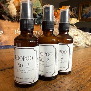 K&ouml;nnte beinhalten: Drei braune Glasspr&uuml;hflaschen mit schwarzen Spr&uuml;hk&ouml;pfen. Jede Flasche hat ein wei&szlig;es Etikett mit dem Text "LOOPOO No. 2", "DOPOO No. 2" und "POO 2". Die Etiketten enthalten auch den Text "Eau de Toilette. W&ouml;rtlich 60ml, ganz nat&uuml;rlich" und "the little soap co."