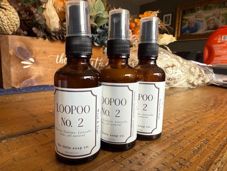 K&ouml;nnte beinhalten: Drei braune Glasspr&uuml;hflaschen mit schwarzen Spr&uuml;hk&ouml;pfen. Jede Flasche hat ein wei&szlig;es Etikett mit dem Text "LOOPOO No. 2", "DOPOO No. 2" und "POO 2". Die Etiketten enthalten auch den Text "Eau de Toilette. W&ouml;rtlich 60ml, ganz nat&uuml;rlich" und "the little soap co."