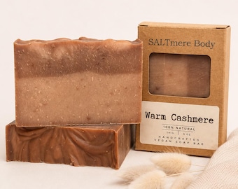 May include: Two rectangular bars of brown soap with a marbled texture, accompanied by a brown cardboard box labeled SALTmere Body Warm Cashmere, 100% natural, 141g, 5 oz, handcrafted vegan soap bar, with a cutout window showing the soap inside.
