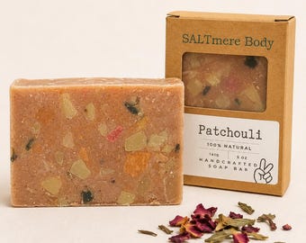 May include: A rectangular bar of soap with a textured, speckled surface in shades of tan and orange, next to its brown cardboard packaging. The box is labeled SALTmere Body Patchouli 100% Natural 141g 5 oz Handcrafted Soap Bar with a peace sign icon.