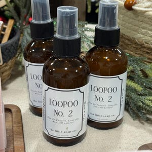 K&ouml;nnte beinhalten: Drei braune Glasspr&uuml;hflaschen mit schwarzen Kappen und wei&szlig;en Etiketten. Die Etiketten lauten "LOOPOO No. 2 Eau de Toilette. W&ouml;rtlich 118ml, ganz nat&uuml;rlich" und "the little soap co."