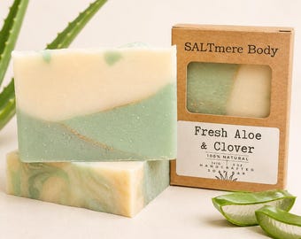 May include: A rectangular bar of soap with a cream and light green marbled design, featuring a thin gold line. It is packaged in a brown cardboard box labeled SALTmere Body Fresh Aloe & Clover 100% Natural Handcrafted Soap Bar 141g 5 oz.