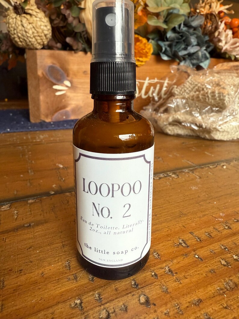 K&ouml;nnte beinhalten: Eine braune Glasspr&uuml;hflasche mit schwarzem Verschluss und wei&szlig;em Etikett. Auf dem Etikett steht "LOOPOO No. 2 Eau de Toilette. Literally 2oz., all natural" und "the little soap co. NEW ENGLAND". Die Flasche steht auf einer Holzoberfl&auml;che.