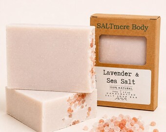 May include: Two rectangular bars of pale lavender soap with embedded pink sea salt crystals, next to a brown cardboard box labeled SALTmere Body Lavender & Sea Salt 100% Natural 155g 5.5 oz Handcrafted Salt Soap Bar with loose salt crystals.