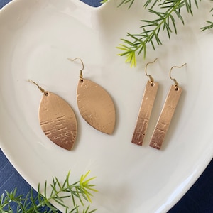 May include: A set of gold-toned earrings. One pair is a leaf shape and the other pair is a rectangular shape.