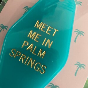 K&ouml;nnte beinhalten: Ein t&uuml;rkisfarbener Motel-Schl&uuml;sselanh&auml;nger mit goldener Aufschrift "Meet me in Palm Springs".