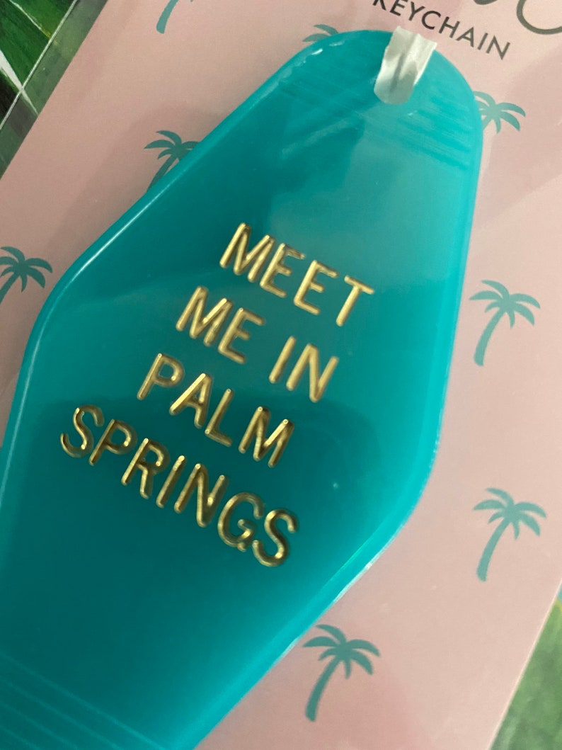 K&ouml;nnte beinhalten: Ein t&uuml;rkisfarbener Motel-Schl&uuml;sselanh&auml;nger mit goldener Aufschrift "Meet me in Palm Springs".
