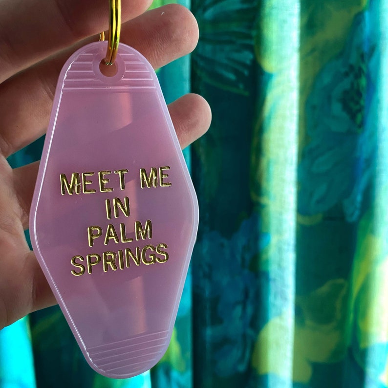 K&ouml;nnte beinhalten: Rosafarbener Motel-Schl&uuml;sselanh&auml;nger mit goldener Aufschrift "Meet Me In Palm Springs".