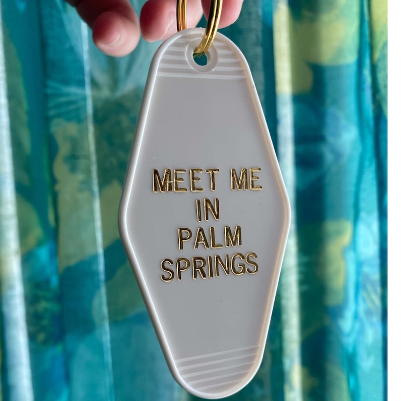 K&ouml;nnte beinhalten: Wei&szlig;er Motel-Schl&uuml;sselanh&auml;nger mit goldener Aufschrift "Meet me in Palm Springs".