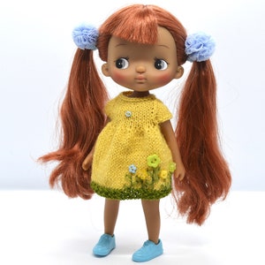 May include: A doll with brown hair and a yellow dress with green trim and blue flowers. The doll is wearing blue shoes.