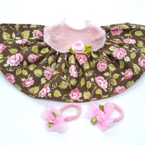 May include: A brown and pink floral doll dress with a pink knitted bodice and two pink hair bows.