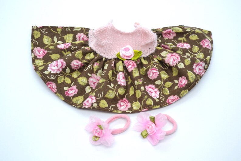May include: A brown and pink floral doll dress with a pink knitted bodice and two pink hair bows.