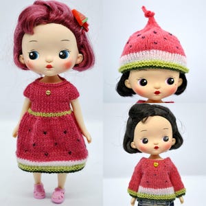 May include: A doll wearing a red knitted dress with a watermelon design, a matching hat, and a red sweater. The dress and sweater have a green and white trim. The doll has red hair and pink shoes.