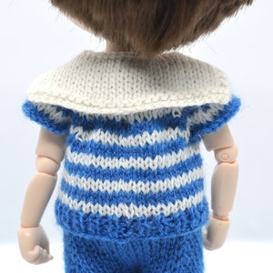 May include: A doll wearing a blue and white striped knitted shirt with a white sailor collar and matching blue pants.