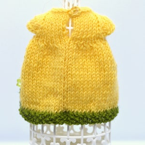 May include: A yellow knitted dress with a green trim. The dress is on a white display stand.
