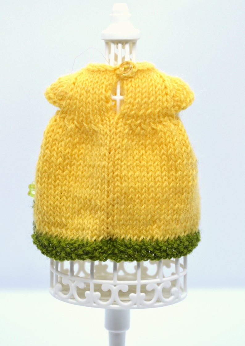 May include: A yellow knitted dress with a green trim. The dress is on a white display stand.