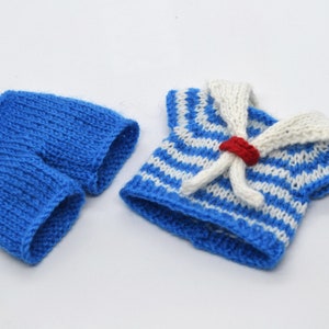 May include: A blue and white striped knitted sailor shirt with a white collar and a red button. The shirt is paired with blue knitted shorts.