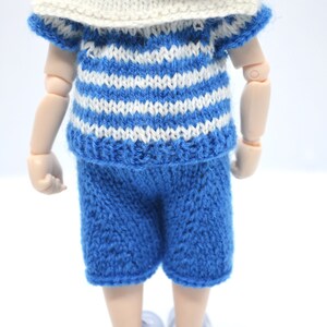 May include: A doll wearing a blue and white striped knitted shirt with a white sailor collar and blue knitted shorts.
