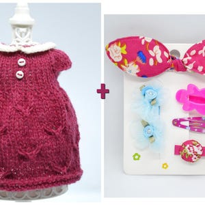 May include: A knitted burgundy dress with a white collar and two buttons. Beside it is a set of hair accessories, including a pink bow with a floral pattern, and several barrettes in pink and blue.