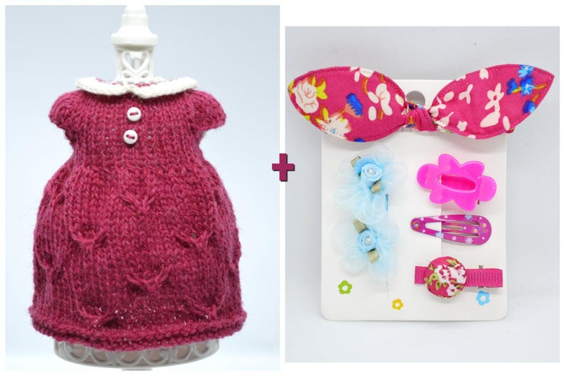 May include: A knitted burgundy dress with a white collar and two buttons. Beside it is a set of hair accessories, including a pink bow with a floral pattern, and several barrettes in pink and blue.