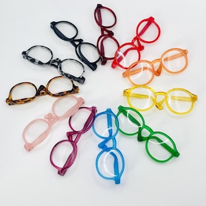 Può includere: Una collezione di occhiali giocattolo colorati disposti a cerchio. Gli occhiali sono disponibili in vari colori, tra cui nero, marrone, rosso, arancione, giallo, verde, blu, rosa e viola. Le montature sono in plastica.