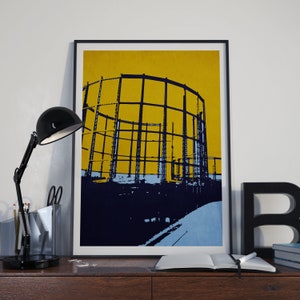 May include: A black framed print of a blue and yellow abstract illustration of a gas holder. The gas holder is a large, cylindrical structure with a series of horizontal bars. The background is a solid yellow color.
