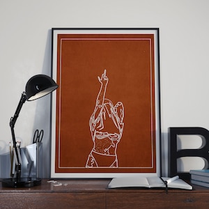 May include: A minimalist line art print of a person with their arm raised in the air, making a middle finger gesture. The print is on a brown background and framed in black.