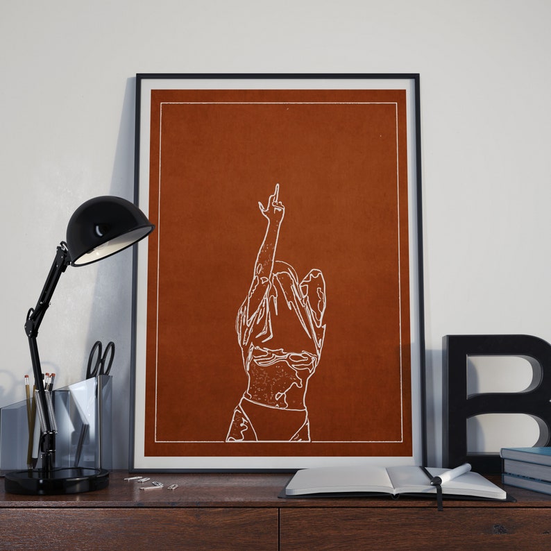 May include: A minimalist line art print of a person with their arm raised in the air, making a middle finger gesture. The print is on a brown background and framed in black.