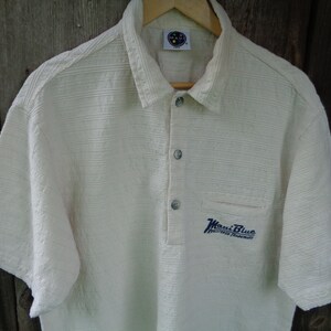 May include: A white short-sleeved polo shirt with a blue embroidered logo that says "Maui Blue" and "Registered Trademark".