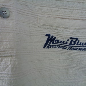 May include: White cotton shirt with a blue embroidered logo that says "Maui Blue Registered Trademark".