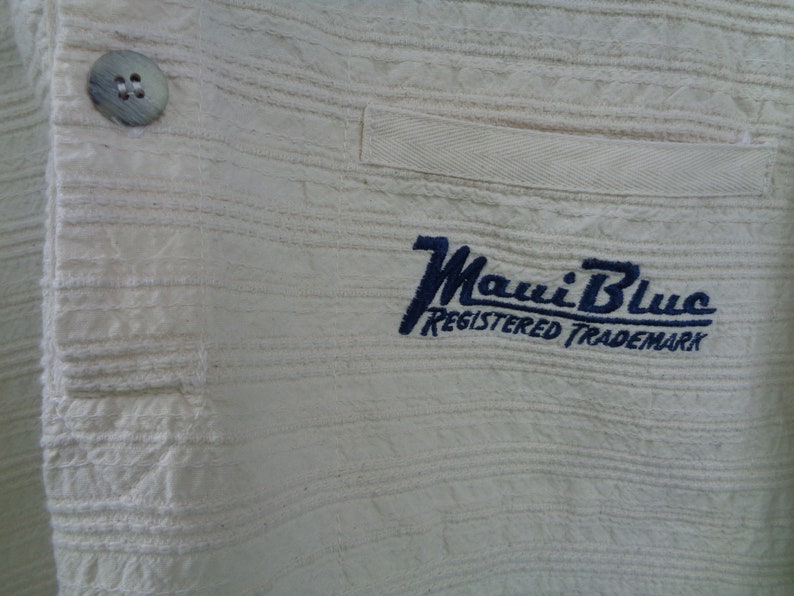 May include: White cotton shirt with a blue embroidered logo that says "Maui Blue Registered Trademark".