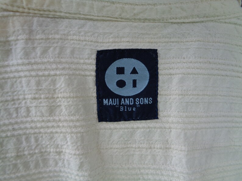 May include: A black label with a white circle, square, and triangle inside. The label says "Maui and Sons" and "Blue" in white text.