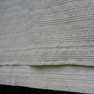May include: Close-up of a white fabric with a textured, ribbed pattern. The fabric is folded in half, showing the texture on both sides.