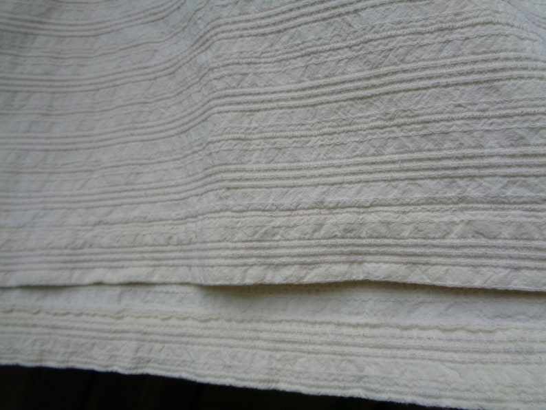 May include: Close-up of a white fabric with a textured, ribbed pattern. The fabric is folded in half, showing the texture on both sides.