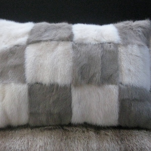 Może przedstawiać: Poduszka z futra w kratkę z naprzemiennymi kwadratami z jasnoszarego i białego futra. Poduszka jest wykonana z miękkiego, pluszowego futra i ma luksusowy charakter.