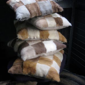 Può includere: Un cumulo di quattro cuscini rettangolari con un design a patchwork di pelliccia marrone, bianca e grigia. I cuscini sono disposti a forma di piramide.