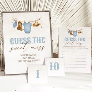 May include: A baby shower game set with a framed sign that reads "GUESS THE sweet mess". The sign has a watercolor illustration of baby clothes. Additional cards and number cards are included, all in a soft blue and white color scheme.
