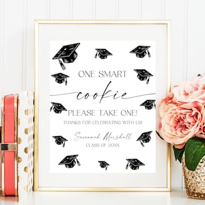 May include: A white sign with black graduation caps and the text "ONE SMART cookie PLEASE TAKE ONE! THANKS FOR CELEBRATING WITH US! Savannah Marshall CLASS OF 20XX"