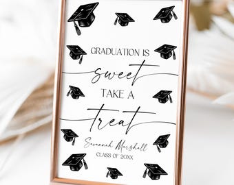 May include: A white sign with a gold frame and black text that reads "Graduation is sweet take a treat Savannah Marshall Class of 20XX". The sign is decorated with black graduation caps.