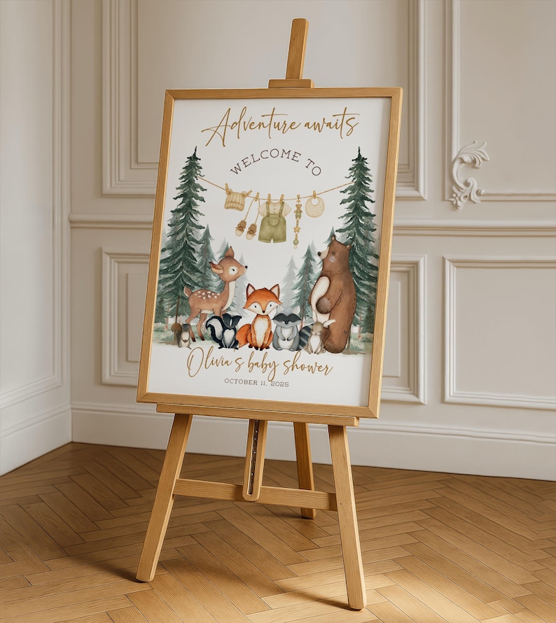 May include: Wooden easel displaying a baby shower sign with the text "Adventure awaits Welcome to Olivia's baby shower October 11, 2022." The sign features watercolor illustrations of forest animals and baby clothes.