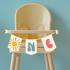 High chair banner spelling out “ONE” with bright sun artwork and bold playful fonts, perfect for first birthday smash cake photo setup.
