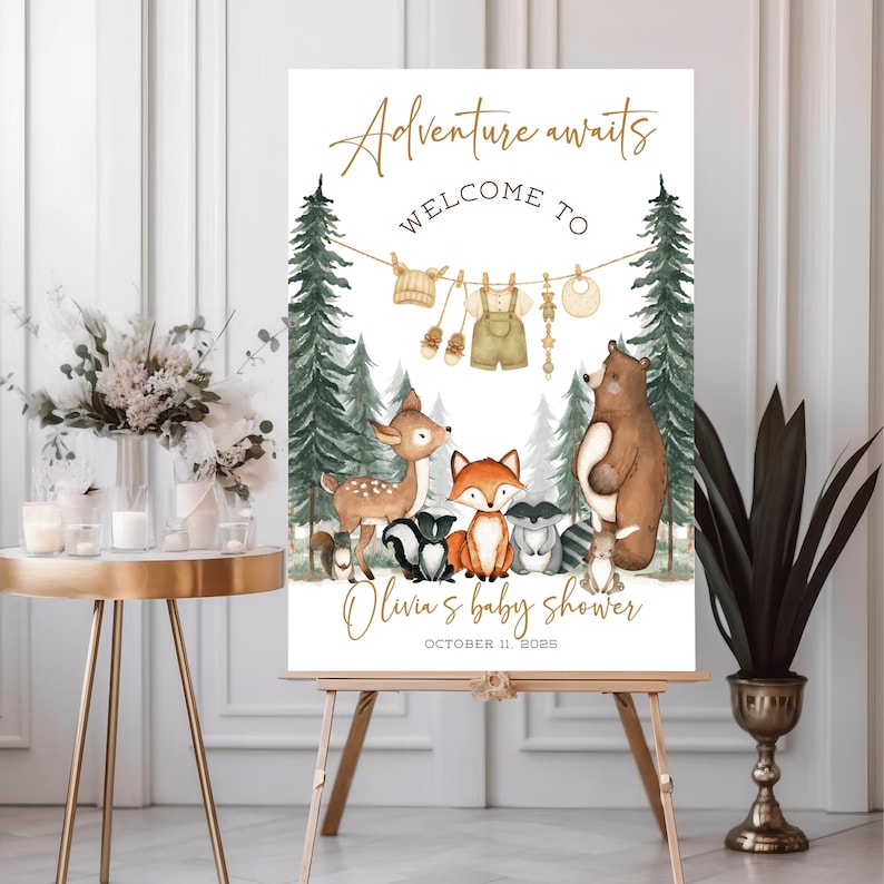 May include: A baby shower welcome sign on an easel. The sign features the text "Adventure awaits" and "Welcome to" in gold script. Below, illustrations of forest animals and baby clothes are displayed. The baby shower is for Olivia, October 11, 2026.