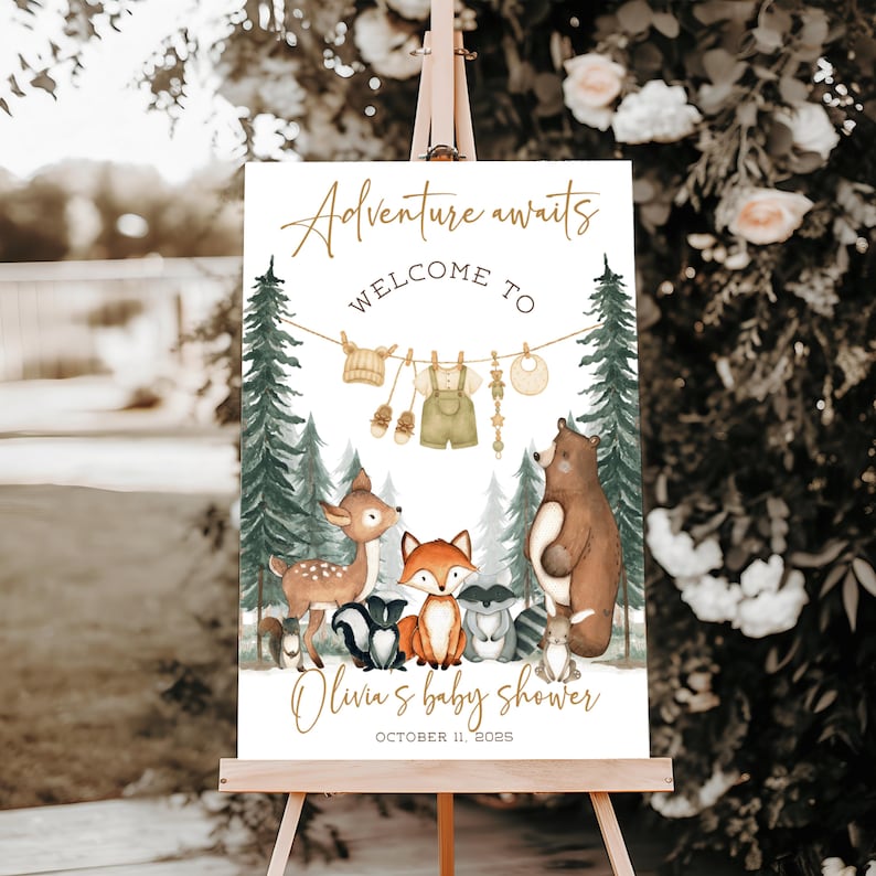 May include: A baby shower welcome sign on an easel. The sign features the text "Adventure awaits" and "Welcome to Olivia's baby shower" with the date. The sign has illustrations of forest animals and baby clothes hanging on a clothesline.