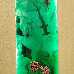 May include: Vertical resin art piece with a vibrant green ocean scene. Features a hammerhead shark, manta ray, octopus, and coral. Driftwood is at the top. The artwork has a glossy finish and is set against a neutral background.