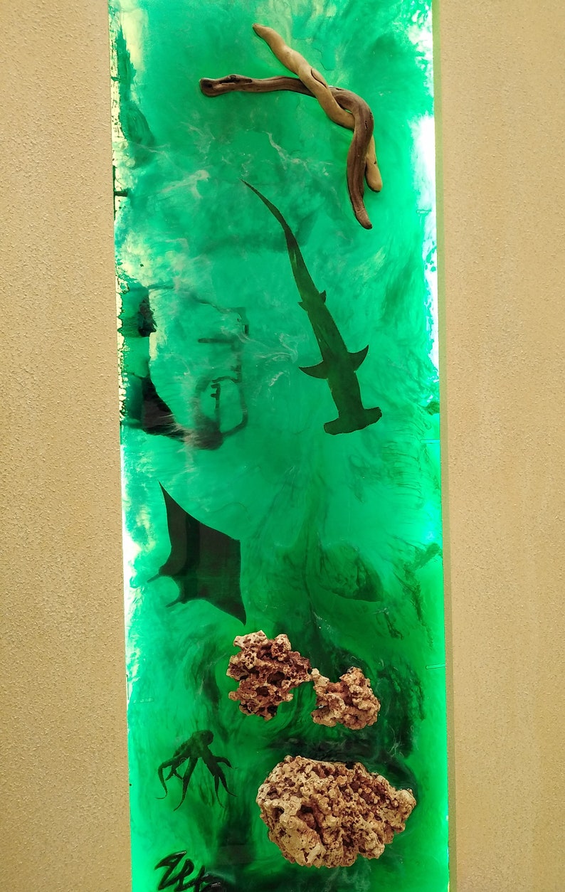 May include: Vertical resin art piece with a vibrant green ocean scene. Features a hammerhead shark, manta ray, octopus, and coral. Driftwood is at the top. The artwork has a glossy finish and is set against a neutral background.