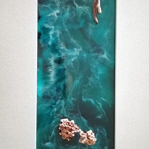 May include: Abstract resin art piece featuring a teal and turquoise ocean scene with a light-colored wooden element and coral-like formations. The artwork is framed in a white mat.
