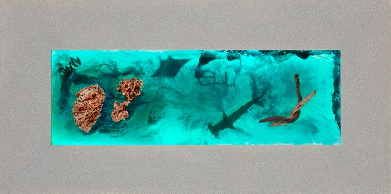 May include: A rectangular artwork featuring an underwater scene with a hammerhead shark, stingrays, and coral. The background is a vibrant turquoise, with a driftwood piece and a gray border.
