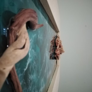 May include: A wooden sculpture of an octopus with a light brown color, mounted on a wall with a blue and white ocean-themed background. A small, textured, coral-like object is also mounted on the wall.